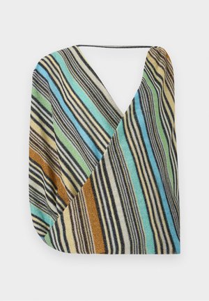 Žena nosiaca bezrukávové, farebné pruhované minišaty s hlbokým výstrihom do V a čiernymi sandálmi na vysokom podpätku, stojaca s rukami za chrbtom.