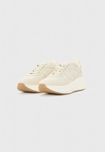 Ζευγάρι εκρού sneakers με πλατφόρμα, μπεζ καουτσούκ σόλες και δέσιμο με κορδόνια σε απλό ανοιχτό γκρι φόντο.