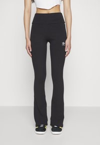 Svarta räfflade utsvängda byxor med hög midja och vit Adidas-logotyp. Tillverkade av ett elastiskt material, designade för komfort och flexibilitet.