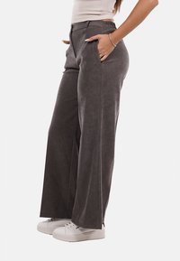 Pantaloni a gamba larga in tessuto grigio scuro con una superficie liscia, dotati di tasche laterali e una cintura elastica. Abbinati a sneakers bianche.