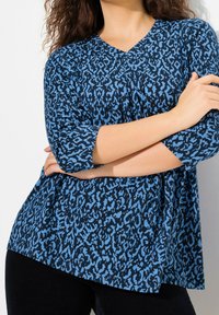 Blå och svart mönstrad skjorta med V-ringning och trekvartärmar, med lös passform och mjuk textur.