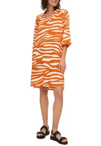Gestreiftes Tunika-Kleid in Orange und Weiß, locker geschnitten mit V-Ausschnitt, drei Viertelärmeln, kombiniert mit schwarzen Plateausandalen.