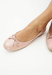 Vaaleanpunaiset ballerinat, jotka on valmistettu kiiltävästä patenttimateriaalista. Ballerinoissa on pyöreä kärki ja etuosassa koristeena nauha. Pintamateriaali on sileää.