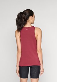 Canottiera atletica senza maniche color bordeaux con scollo rotondo e una texture liscia, abbinata a pantaloni ciclistici neri con motivo, vista da dietro.