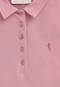 Rosa pikétröja med strukturerat tyg, fem knappar och en liten broderad figur. Etikett med texten "POLO CLUB," storlek Medium.