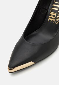 Décolleté nera in pelle con tacco alto, punta affusolata e punta accentuata in oro. Presenta una finitura testurizzata e un logo impresso sul lato.