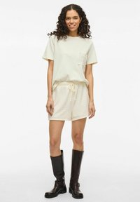 Camiseta de manga corta color crema claro con un bolsillo, combinada con pantalones cortos texturizados color crema y botas de cuero marrón hasta la rodilla.