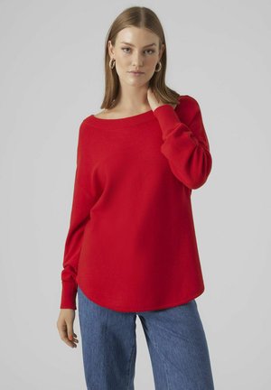 Röd långärmad tröja med vid halsringning, ribbade muddar och lös passform. Kombinerad med blå vida jeans för kontrast.