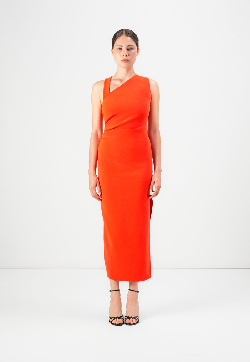 Frau steht in einem taillierten, ärmellosen, hellorangefarbenen Midikleid mit asymmetrischem Ausschnitt und schwarzen, geschnürten High Heels.