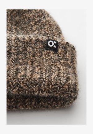 Berretto lavorato a maglia in tonalità di marrone con un aspetto texturizzato e peloso. Presenta un'etichetta nera con un logo bianco sul lato.