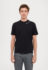T-shirt in cotone nero con maniche corte e collo a girocollo. Presenta un piccolo logo bianco sulla spalla sinistra e una vestibilità standard.