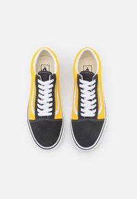 Sorte og gule skate sko har en overdel i lærret, hvite snørebånd, kontrasterende gamasjer foran, og en klassisk hvit side stripe.