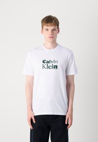 Hvit bomulls t-skjorte med en grønn "Calvin Klein" logo i fet typografi. Korte ermer, rund hals, avslappet passform.