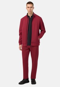 Chaqueta burdeos con cremallera y cuello negro, combinada con pantalones tapered a juego. Ambos tienen una textura suave y un diseño minimalista. Zapatillas negras incluidas.