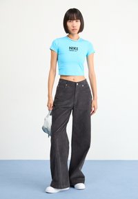 Light blue cropped Nike t-shirt with black logo, paired with wide-leg charcoal pants and white sneakers. Holds a small gray bag.