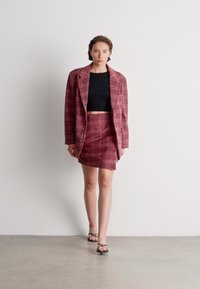 Divdaļīgs uzvalks burgundijas krāsā ar pārbaudi. Žakete ar izgrieztiem uzliekamajiem klātnes un strukturētu piegriezumu, kopā ar pieguļošu, ceļa garuma svārku.