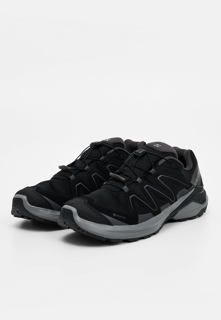 Par de zapatos deportivos de senderismo en negro y gris con tela Gore-Tex y sistema de cordones rápidos, exhibidos sobre fondo blanco.