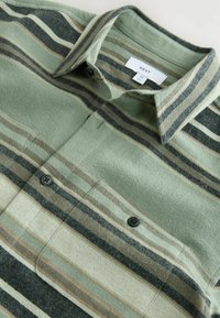 Buttoned green and beige striped flannel shirt with a collar and black buttons, labeled size medium by Next brand.
