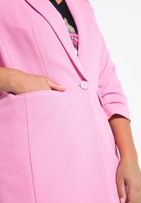 Blazer rosa hecho de tejido suave. Presenta un cierre de un solo botón y bolsillos laterales. Cuello de chal y mangas tres cuartos.