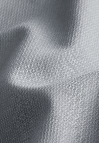 Világosszürke szövet texturált felülettel, finom mintázattal, lágy redőkkel és árnyékokkal. Simaság és hajlékonyság jellemzi az anyagot.