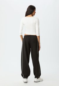 Witte, aansluitende top met driekwart mouwen en zwarte, loszittende broek met witte zijstrepen. De broek heeft een elastische tailleband en omgeslagen zoom.