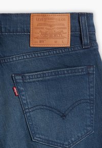 Zadní kapsa modrých džínsů Levi's 511 s viditelným šitím, červenou značkou Levi's a hnědým koženým štítkem obsahujícím informace o značce a velikosti.
