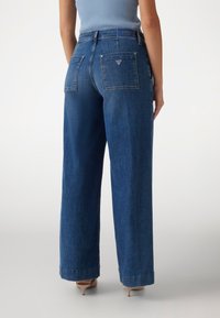 Weite Jeans in dunkelblauem Denim, mit hoher Taille, zwei Gesäßtaschen und einem kleinen dreieckigen Logo am Bund.