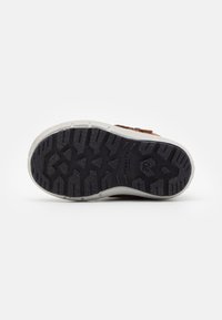 Braune Turnschuh-Außensohle mit strukturiertem schwarzem Gummi für Traktion, ausgestattet mit einer weißen Zwischensohle und geprägtem Markenlogo an der Seite.