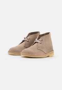 Stivali ankle in suede beige con punta rotonda, lacci in pelle e suola in gomma leggera. Presentano dettagli cuciti vicino alla suola.