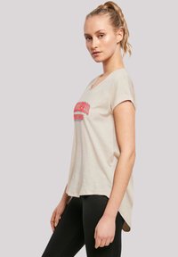 Beige cotton t-shirt with short rolled sleeves, rounded neckline, featuring red text "Morris" on the front, slightly longer back hem.