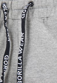 Grijze trainingsbroek van een gestructureerde stof met een zwart trekkoord, geaccentueerd door "GORILLA WEAR" in het wit gedrukt.