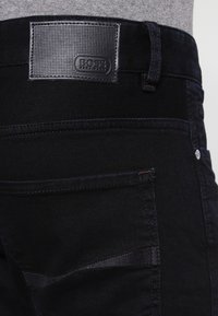 Czarne dżinsy z denimu z fakturowaną, czarną skórzaną naszywką z logo marki, metalowym guzikiem oraz subtelnymi detalami przeszycia na kieszeniach.