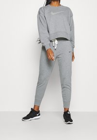 Grauer Sweatshirt mit einem verkürzten Design und einem silbernen Nike-Logo, kombiniert mit passenden grauen Jogginghosen mit einem Kordelzug und schwarzen Sneakers.