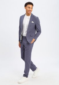 Marineblauw pak van gestructureerde stof, met een getailleerde blazer met notch revers, gecombineerd met bijpassende broek en een wit shirt.