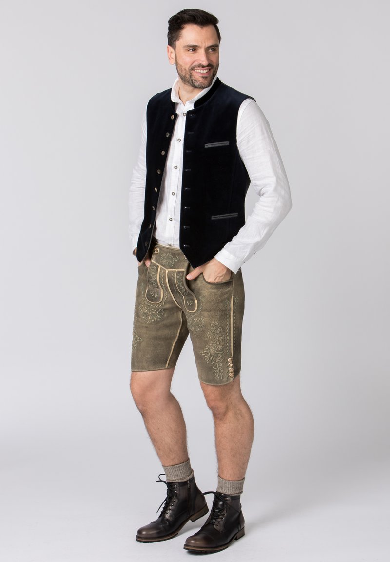 Traditioneel Beierse outfit met een donker fluwelen gilet, een wit hemd met knopen en knielange shorts met bloemmotieven, in beige geaccentueerd.
