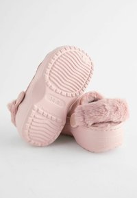 Sabots roses avec une sangle en fourrure douce, semelle en caoutchouc texturé et coussin de pieds rond. Comprend une boucle sécurisée et un détail de taille en relief.