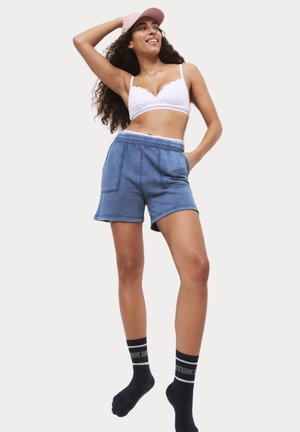 Ljusblå bomullsshorts med elastiskt midjeband, två sidofickor, kombinerat med en vit spetsbralette och svarta strumpor med text.