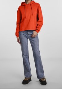 Röd kort hoodie med snörning, matchad med ljusblå utsvängda jeans och svarta platåskor. Slät tygkvalitet och avslappnad passform genom hela plagget.