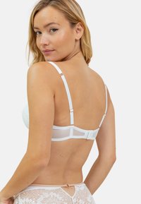 Bralette blanche avec des détails en dentelle, des bretelles réglables et une fermeture à crochets et œillets dans le dos. Le tissu semble doux avec un motif floral délicat.