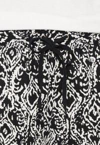 Svartvitt mönstrat tyg med en intrikat blommönster. Har en dragsko i midjan och en strukturerad yta.