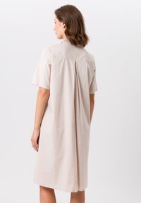 Robe courte à manches courtes beige clair avec une coupe droite, dotée d'un pli au dos, d'un col et en tissu de coton lisse.