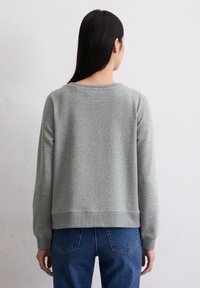 Sudadera gris con escote redondo, puños y dobladillo de canalé, y un ajuste relajado. Combinada con jeans de denim azul. Textura de tela suave.