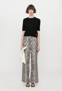 Top nero a maniche corte abbinato a pantaloni a gamba larga con una stampa a serpente in toni beige e grigi. Tessuto bianco drappeggiato a mano.