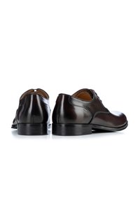 Zapatos de vestir de cuero marrón con un acabado suave, punta redondeada y un tacón bajo, presentan costuras mínimas y sin hardware visible.