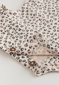 Tissu beige doux avec imprimé léopard noir et rose et deux boutons marron sur les bords pliés.