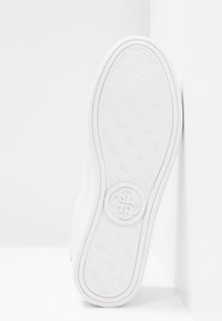 Semelle de sneaker blanche avec un motif texturé et un logo circulaire au centre. Bord arrondi avec un rebord extérieur renforcé. Matériau lisse et flexible.