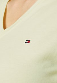 T-Shirt mit V-Ausschnitt und kurzen Ärmeln aus leichtem grünen Baumwollstoff, mit einem kleinen, gestickten Logo in Rot, Weiß und Marineblau auf der Brust.
