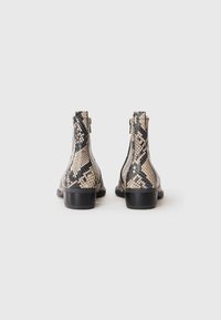 Botas de tobillo con estampado de piel de serpiente en beige y negro, que presentan una cremallera lateral, puntera redonda y tacón bajo.