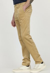 Pantalons en velours côtelé beige avec une texture côtelée verticale, coupe slim et poches avant. Portés avec des baskets claires.