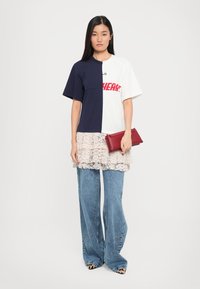 Kleur-geblokte T-shirt in navy en wit met een grafische print. Laagjes van kantrok met een golvende textuur, gecombineerd met wijde denimbroeken en een rode clutch.